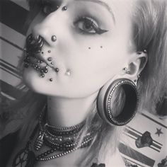 a black and white photo of a woman with piercings on her nose, wearing large hoop earrings