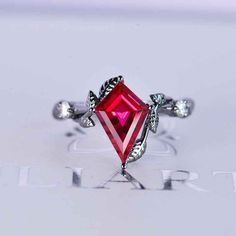 a red diamond ring with leaves on the sides and diamonds around it, sitting on top of