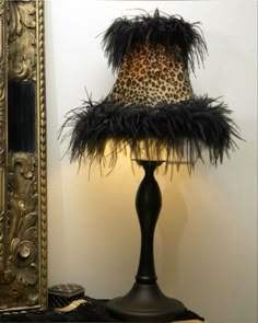 a lamp with a leopard print shade on it next to a mirror and a gold frame