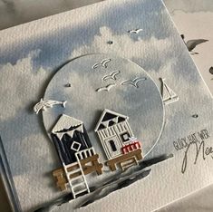 a close up of a card with a house on the beach and seagulls flying around