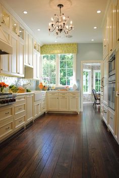 a large kitchen with wooden floors and white cabinets, chandelier hanging from the ceiling