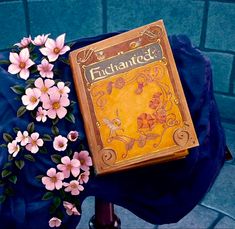 a book with flowers sitting on top of it next to a blue cloth covered chair