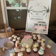 a table topped with lots of cupcakes next to a welcome sign