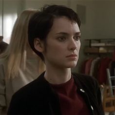 a woman with short hair standing in front of a clothing rack and looking off to the side