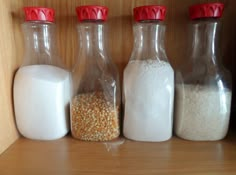 three glass bottles filled with different types of food on a wooden shelf next to each other