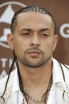 a man with dreadlocks on his head wearing a white shirt and long necklace