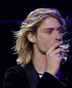 a young man with long hair is holding his hand to his mouth