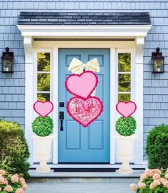 a blue front door decorated with hearts and potted plants on either side, along with two white planters filled with pink flowers