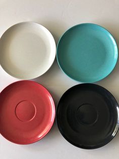 four different colored plates sitting next to each other on a white table top with one black, one red and one blue