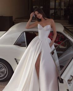 a woman standing next to a white car in front of a building wearing a dress