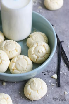 a blue bowl filled with white cookies next to a glass of milk