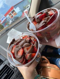 two plastic cups filled with chocolate and strawberries on top of a car dash board