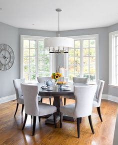 a dining room table with white chairs and a clock on the wall