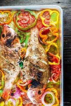 two raw fish in a container with colorful vegetables and seasonings on the side, ready to be cooked