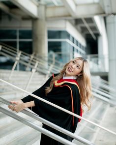 a woman in graduation gown standing on the stairs smiling at the camera with her arms outstretched