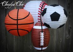 two paper lanterns with soccer, basketball and football ball decorations hanging from the side of a wooden fence