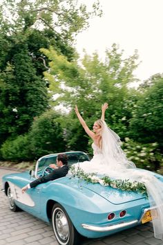 a bride and groom are riding in the back of a blue car with greenery on top