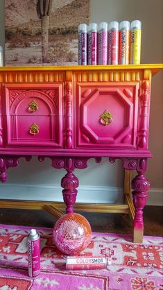 a pink and yellow dresser with lots of paint on it's sides, in front of a painting