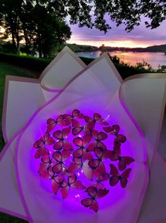 a large purple flower with lots of pink butterflies on it's petals in front of a body of water