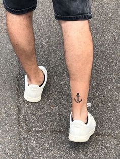 a man's foot with an anchor tattoo on his left leg and white shoes