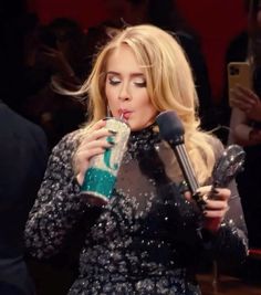 a blonde woman drinking from a cup while standing in front of a microphone and talking on the phone