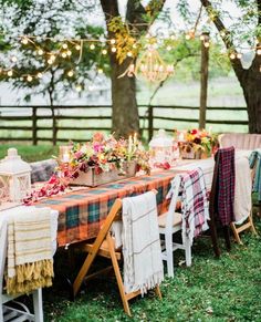 an outdoor table set up with plaid cloths and flowers on it, surrounded by string lights