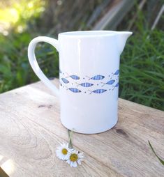 a blue and white pitcher sitting on top of a wooden table next to daisies