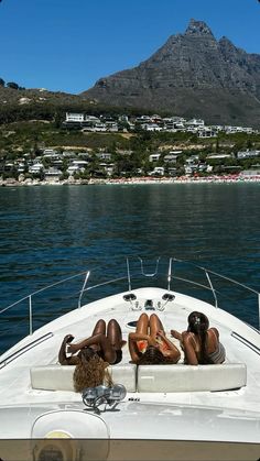 two women lounging on the back of a boat in front of a mountain range