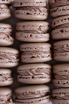 many chocolate macaroons are stacked on top of each other and have frosting