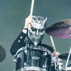 a man with white makeup on his face and head playing drums in front of him