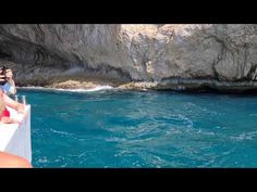 two people on a boat in the water near some cliffs and blue water, with one person taking a photo