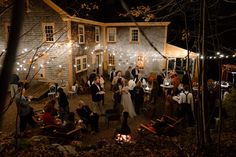 a group of people standing in front of a house at night with string lights on