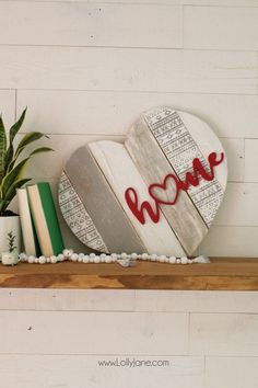 a wooden heart with the word love painted on it next to books and potted plants