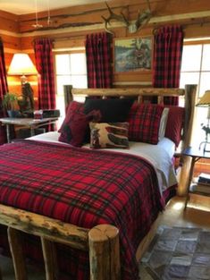 a bed with red and black plaid comforter in a cabin style bedroom, along with two lamps on either side of the bed