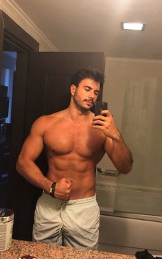 a shirtless man taking a selfie in the bathroom mirror with his cell phone