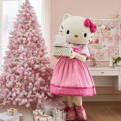 the hello kitty doll is holding a present in front of a pink christmas tree with presents