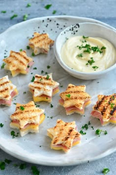 small sandwiches on a plate next to a bowl of dip