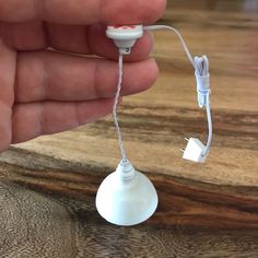 a hand holding a white light bulb on top of a wooden table next to a cord