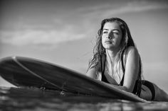 a woman sitting on top of a surfboard next to the ocean in black and white