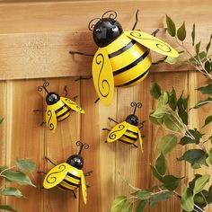 four yellow and black bees are hanging on a wooden wall next to green leaves in the foreground