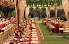 a long table set up with red and gold place settings for an outdoor wedding reception