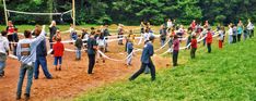 a group of people standing on top of a lush green field next to a forest