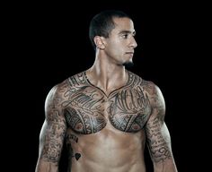 a man with lots of tattoos on his chest and arms, standing in front of a black background