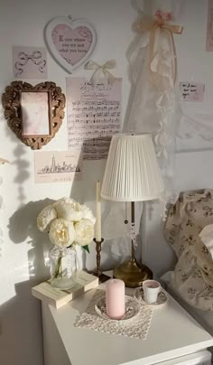 a white table topped with a lamp next to a vase filled with flowers and candles