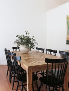 a wooden table surrounded by black chairs and a vase with a plant on top of it