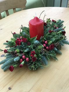 a candle sits on top of a table with greenery and berries