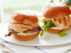 two chicken sandwiches on buns with lettuce and tomato sauce are sitting on a white plate