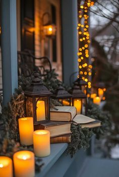 some lit candles are sitting on a porch ledge with books and christmas lights in the background