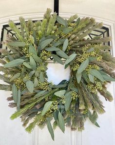 a wreath is hanging on the front door with green leaves and greenery around it