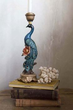 a blue peacock statue sitting on top of a book next to a lit candle holder